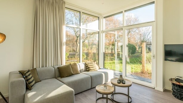 A modern living room with a sectional sofa, two small round tables, and large windows offering a view of a garden.