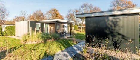 Et moderne etplanshus med en overdækket terrasse og et lille skur.