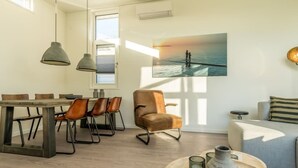A modern living room with a dining area, a large window, and a painting of a sunset over water.