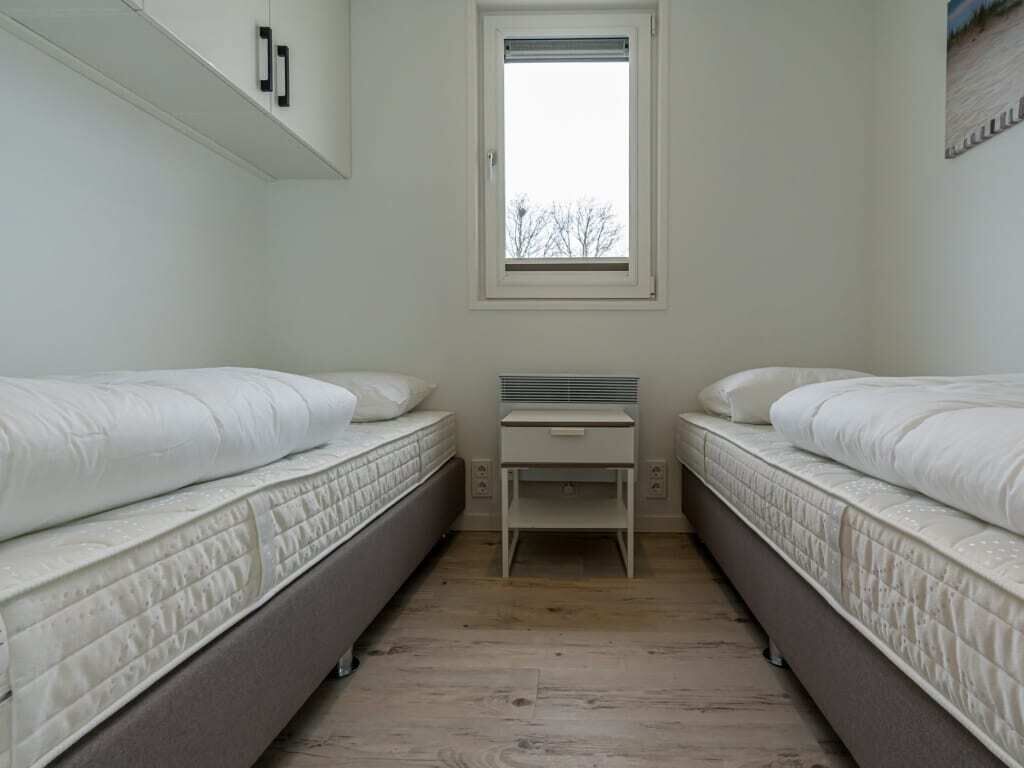 Een kleine, smalle kamer met twee éénpersoonsbedden, een tafeltje en een raam.