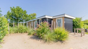 A modern building with large windows, surrounded by greenery and a gravel path. - What immediately catches your eye upon entering is the garden-oriented living room with open kitchen (Burgh-Haamstede)