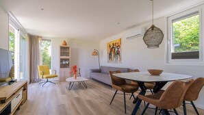 A modern living room with a sofa, dining table, and chairs, a TV, and a bookshelf. - What immediately catches your eye upon entering is the garden-oriented living room with open kitchen (Burgh-Haamstede)