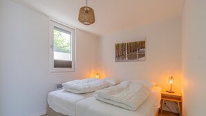 A bedroom with two beds, a window, a wall-mounted picture, and a bedside lamp. - What immediately catches your eye upon entering is the garden-oriented living room with open kitchen (Burgh-Haamstede)