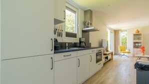 A modern kitchen with white cabinets, a coffee maker, and a dining area with a yellow chair and a table. - What immediately catches your eye upon entering is the garden-oriented living room with open kitchen (Burgh-Haamstede)