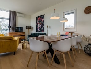 Uma sala de estar moderna com uma mesa de jantar de madeira, cadeiras brancas, um sofá amarelo e uma televisão.