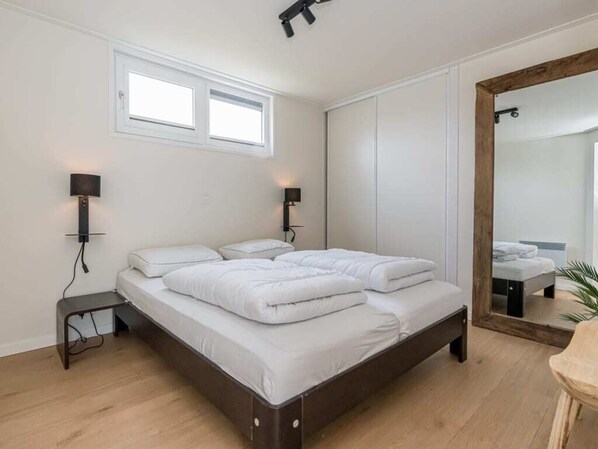 A bedroom with a bed, bedside lamps, a mirror, and a window. - This attractive chalet is located in a beautiful location at the back of Schouwenduin, surrounded by (Burgh-Haamstede)