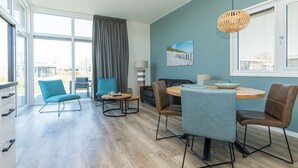 A modern living room with a dining area, large windows, and a view of the city. - This modern chalet with 'Beach style' finish is located on a spacious plot and suitable for 4 people (Burgh-Haamstede)