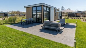 A modern building with a patio area featuring a table, chairs, and a bench. - This modern chalet with 'Beach style' finish is located on a spacious plot and suitable for 4 people (Burgh-Haamstede)