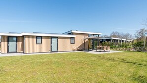 Ein modernes Gebäude mit flachem Dach, großen Fenstern und einem grünen Rasen.