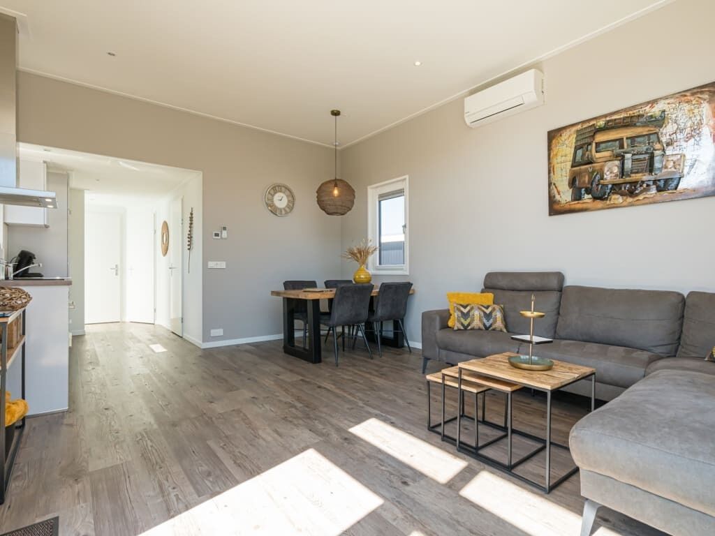 A modern living room with a grey sofa, wooden coffee table, and a dining area with a table and chairs.