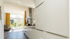 Eine moderne Küche mit weißen Schränken, einer Edelstahl-Dunstabzugshaube und einem großen Fenster mit gelben Vorhängen.