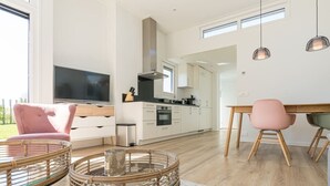 A modern kitchen with white cabinets, a large TV, and a dining area with a table and chairs. - This attractive chalet is located on a spacious plot and is suitable for 4 people. The garden, laid (Burgh-Haamstede)