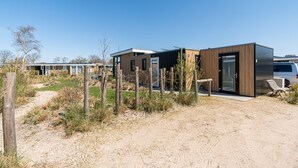 Un camping moderne doté de plusieurs caravanes, chacune ayant une entrée distincte et un petit espace extérieur aménagé pour s’asseoir.