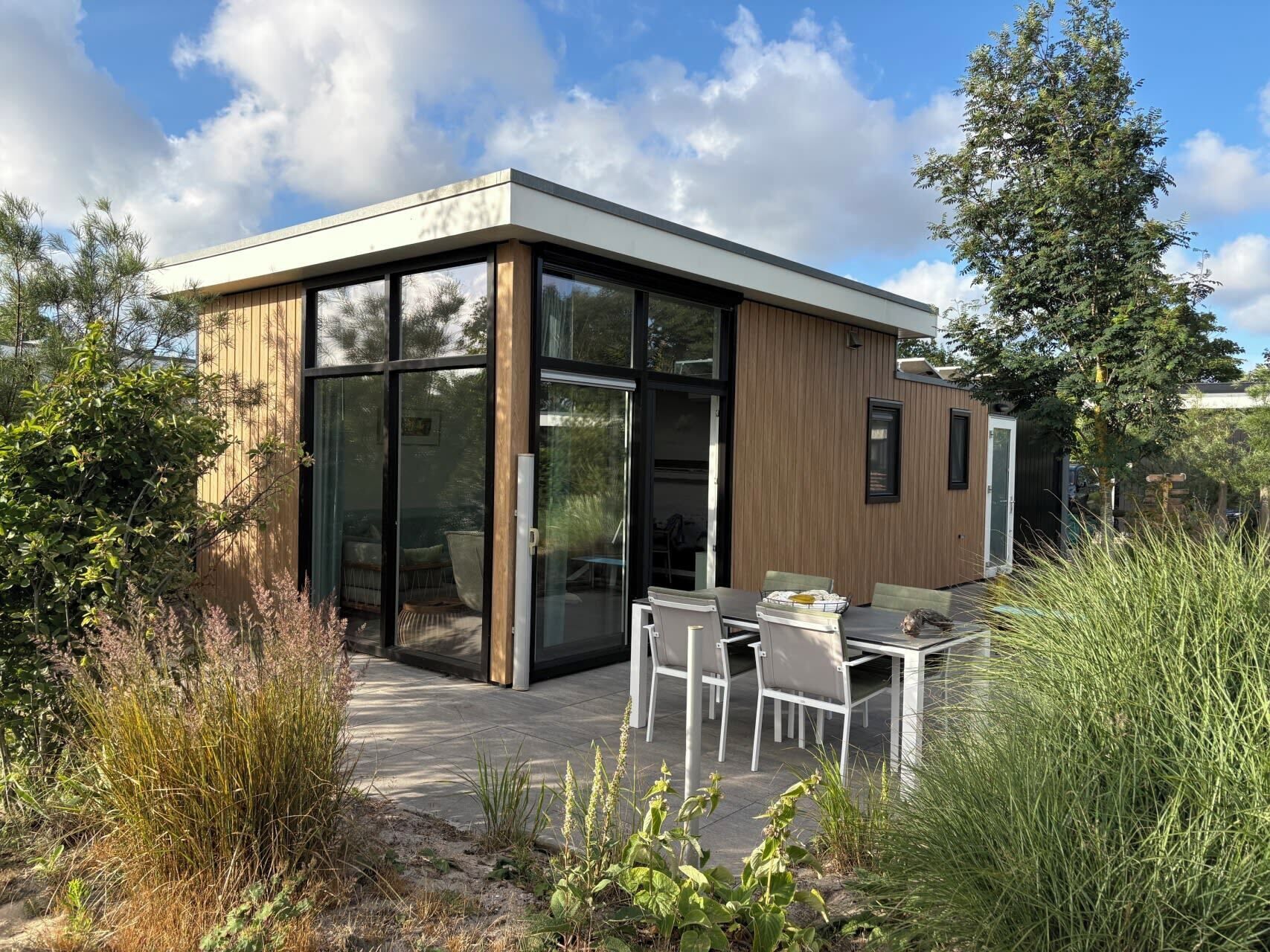 A modern house with a glass door entrance, a patio with a table and chairs, and a wooden exterior.