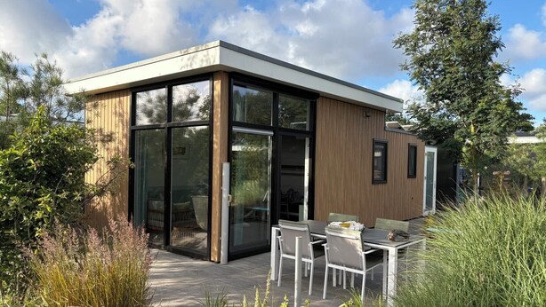 Une maison moderne avec une entrée dotée d’une porte en verre, un patio avec une table et des chaises, et une façade en bois.