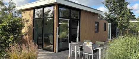 A modern house with a glass door entrance, a patio with a table and chairs, and a wooden exterior.
