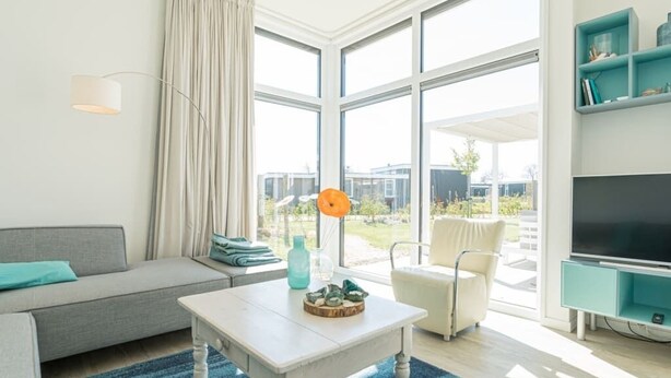 A modern living room with a sofa, a coffee table, and a TV. There is a large window providing a view of the outdoors. - Fan of Ibiza "style"? Then we can assure you that you will feel at home here! Via the shell path and (Burgh-Haamstede)