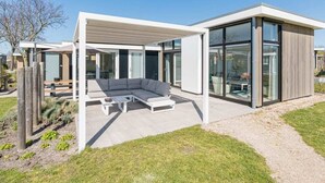 A modern house with a covered outdoor seating area, large glass windows, and a minimalist design. - Fan of Ibiza "style"? Then we can assure you that you will feel at home here! Via the shell path and (Burgh-Haamstede)