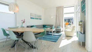 A modern living room with a round wooden table, teal and gray chairs, a gray sofa, and a blue rug. - Fan of Ibiza "style"? Then we can assure you that you will feel at home here! Via the shell path and (Burgh-Haamstede)