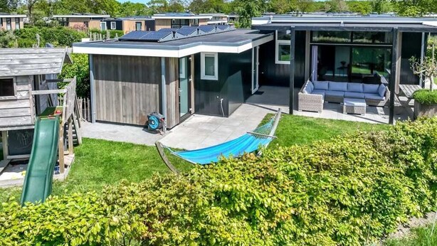 A modern house with a solar panel roof, a covered patio, and a hammock.