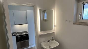A compact kitchen with a stove, oven, and cabinets, a white sink with a mirror above, and a small window.
