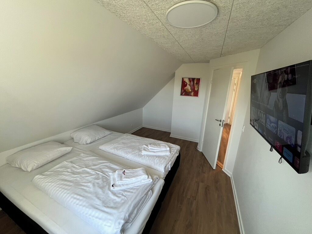 A bedroom with two beds, a flat-screen TV mounted on the wall, and a door leading to another room.