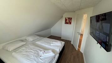 A bedroom with two beds, a flat-screen TV mounted on the wall, and a door leading to another room.