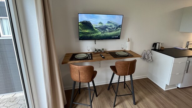 Eine moderne Küche mit Essbereich, einem an der Wand befestigten Fernseher und einem Fenster mit Vorhängen.