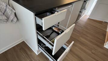A compact kitchen with a black countertop, white cabinetry, a built-in oven, and a stainless steel kettle.
