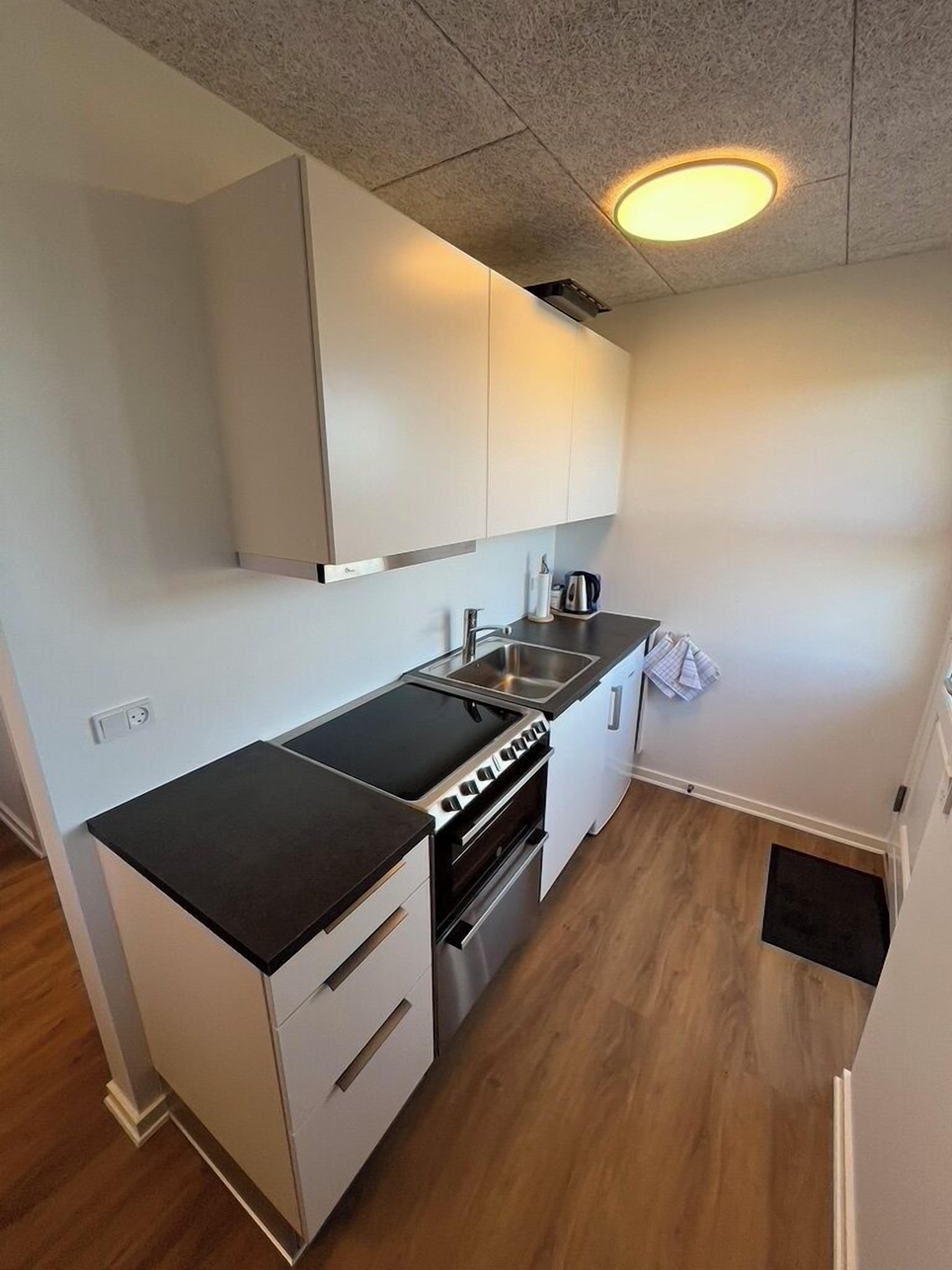A compact kitchen with white cabinets, a black countertop, stainless steel appliances, and a recessed ceiling light.