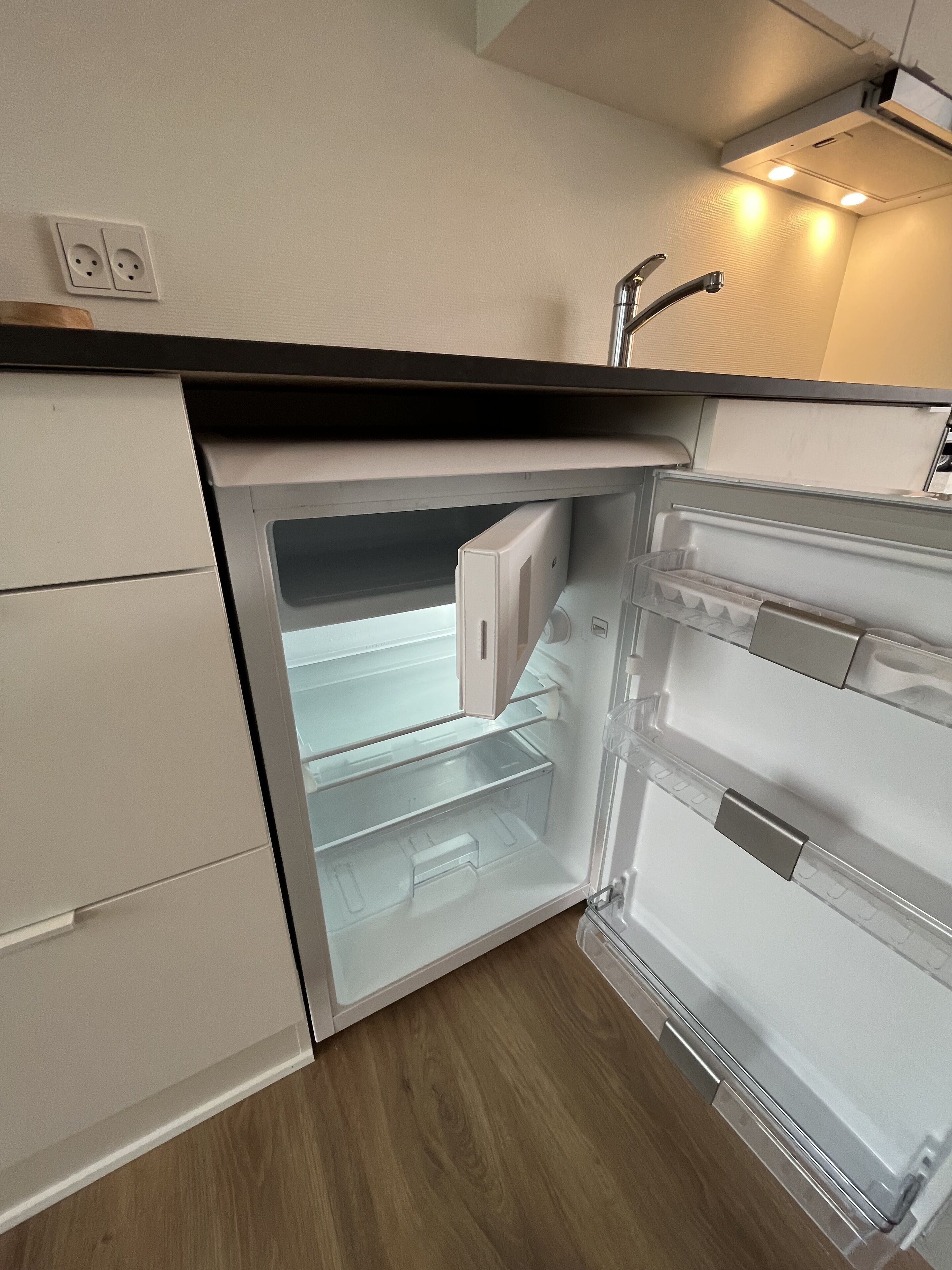 Eine kleine Küche mit integriertem Kühlschrank, Spüle und Arbeitsplatte.