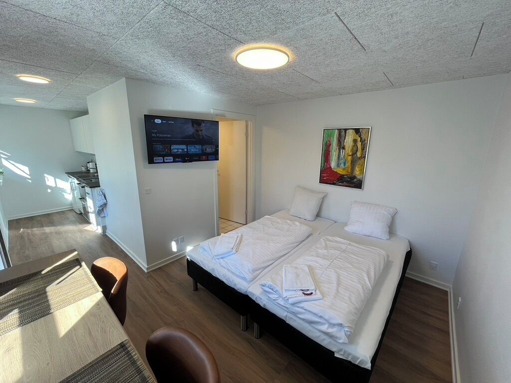 Una habitación de hotel moderna con una cama grande, un televisor de pantalla plana montado en la pared y un cuadro sobre la cama.