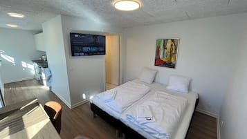 Una habitación de hotel moderna con una cama grande, un televisor de pantalla plana montado en la pared y un cuadro sobre la cama.