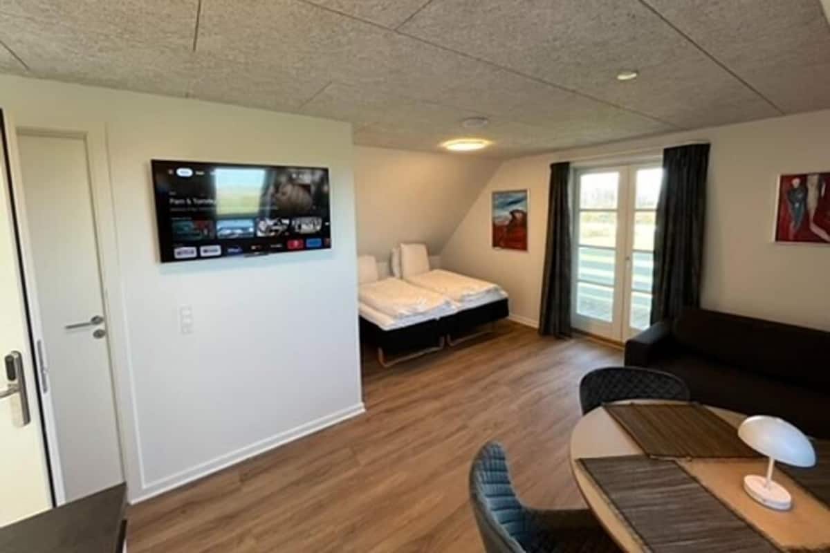 A compact room with a bed, a desk, a chair, and a television mounted on the wall.