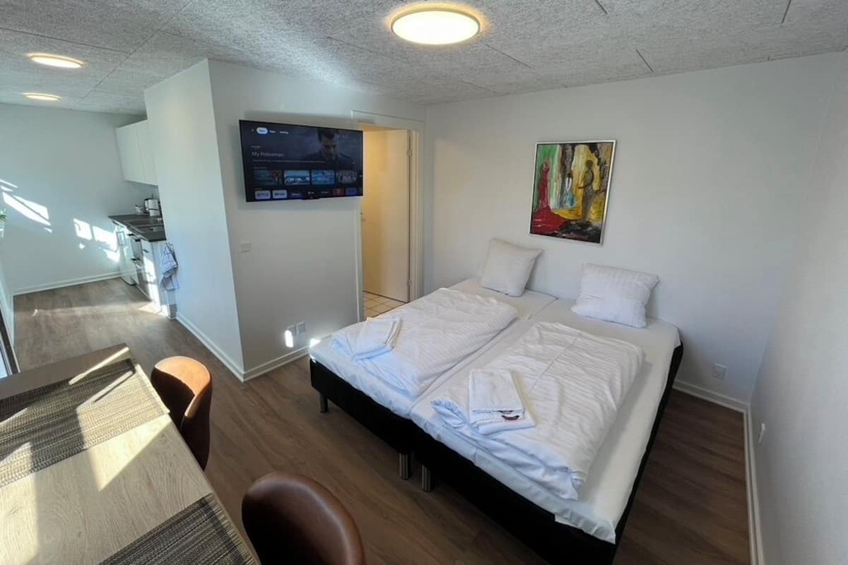 A modern hotel room with a large bed, a flat-screen TV mounted on the wall, and a painting above the bed.