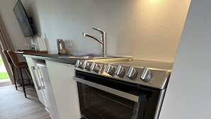 Eine moderne Küche mit Einbauofen, Edelstahlspüle und einem Wand-Fernseher.
