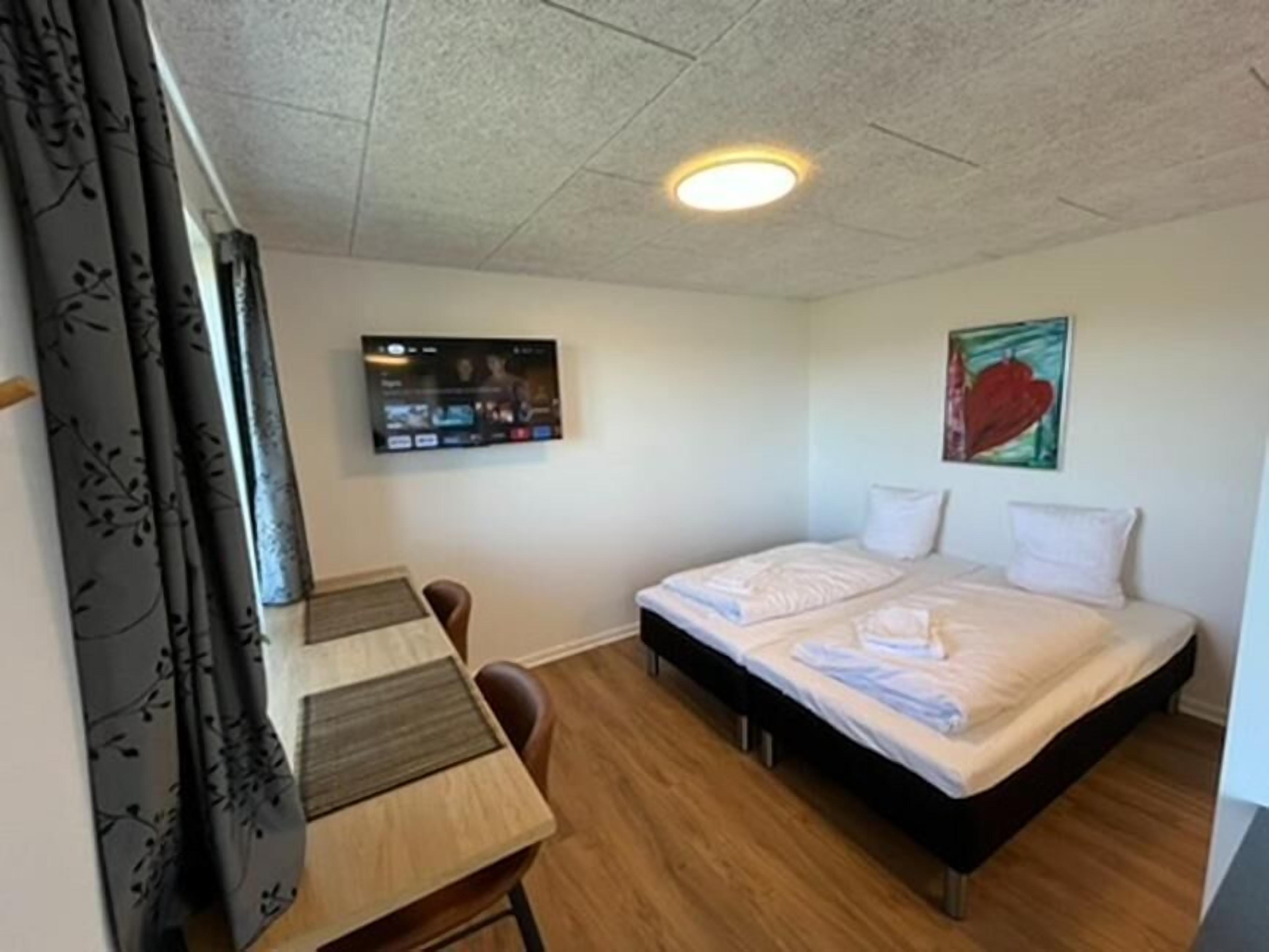 Ein kleines, sauberes Zimmer mit einem Bett, einem Schreibtisch und einem Fernseher.