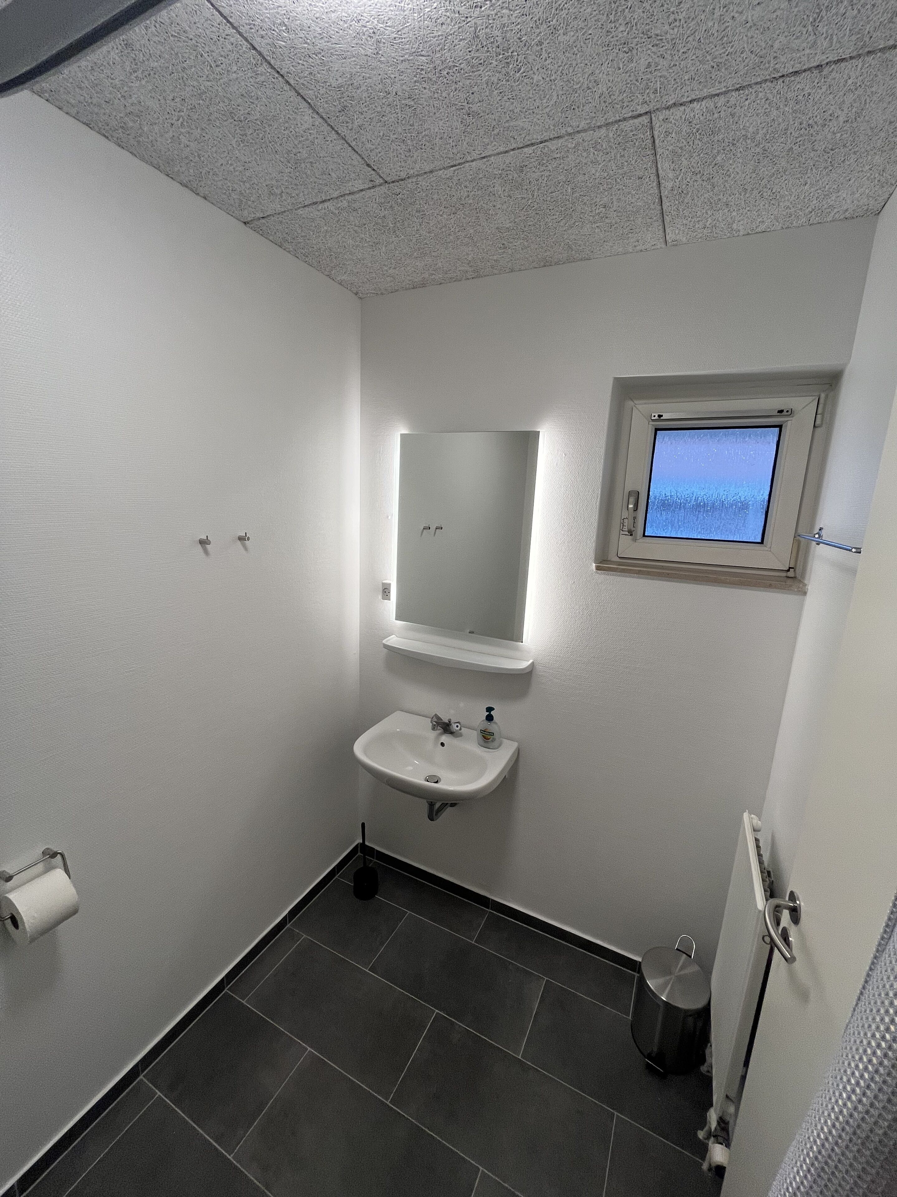 A small, clean bathroom with a white sink, a mirror, and a window.