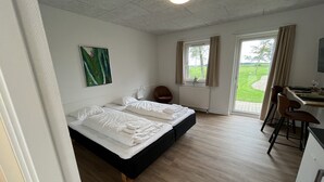Ein Schlafzimmer mit einem Bett, einem Schreibtisch und einem Stuhl. Ein Fenster mit Vorhängen bietet einen Blick ins Freie.