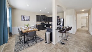 A modern kitchen with dark cabinets, a central island, and a dining area with a table set for four. - Near IAH Houston Home | Yard BBQ Games Wi-Fi Pets (Houston)