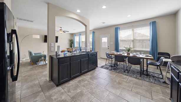 A modern kitchen with a central island, dining area with chairs and a table, and a living space with a sofa and a TV. - Near IAH Houston Home | Yard BBQ Games Wi-Fi Pets (Houston)