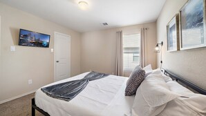 A bedroom with a bed, a cityscape TV, a door, and a window with blinds. - Near IAH Houston Home | Yard BBQ Games Wi-Fi Pets (Houston)