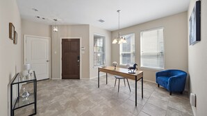 A spacious room with a wooden dining table, two chairs, a blue armchair, and a glass coffee table. - Near IAH Houston Home | Yard BBQ Games Wi-Fi Pets (Houston)