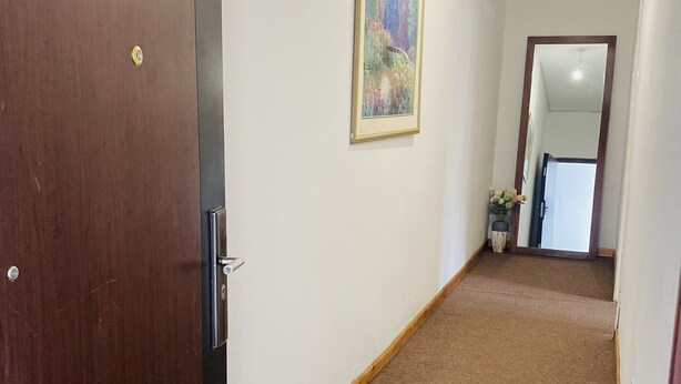Un couloir avec une porte en bois, un tableau encadré accroché au mur et un sol recouvert d’une moquette.