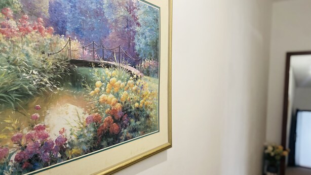 Ein gerahmtes Gemälde einer Brücke über einem Gewässer mit bunten Blumen am Ufer.