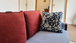 Ein Sofa mit roten und blauen Kissen, ein gemustertes Kopfkissen und eine schlichte Wand mit zwei Türen im Hintergrund.