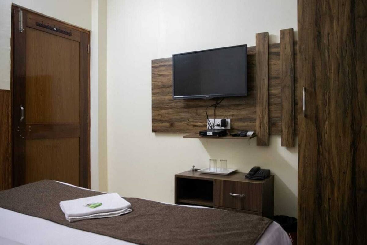 A hotel room with a bed, a TV mounted on the wall, a wooden cabinet, and a door.