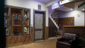 A modern living room with a wooden floor, a dark brown leather sofa, a patterned rug, a staircase, and a door with a glass panel. - Home Stay Green View Doon (Dehradun)