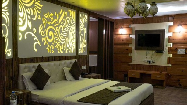 A hotel room with a large bed, a TV mounted on the wall, and a decorative light panel. - Home Stay Green View Doon (Dehradun)