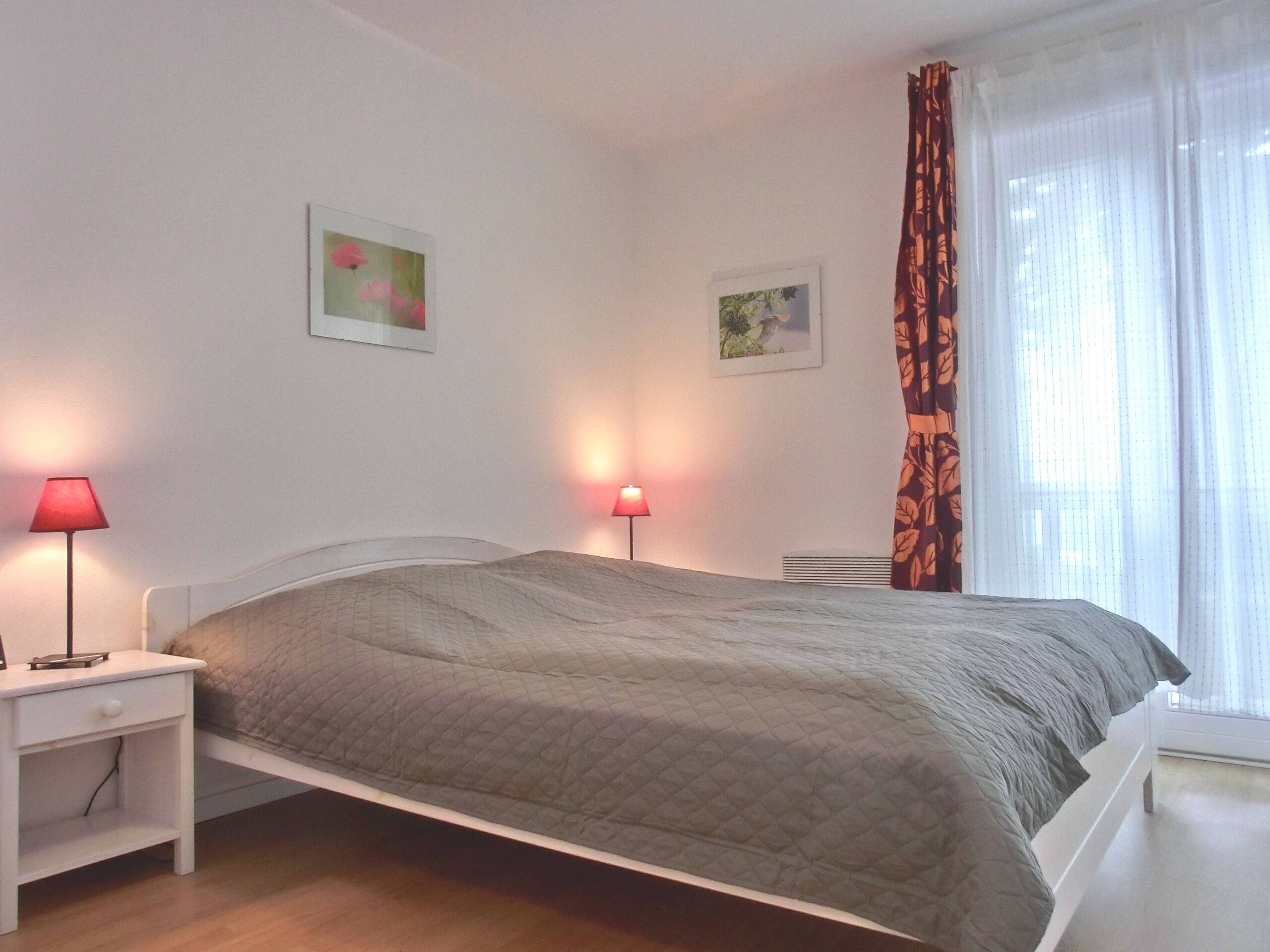 Ein ordentlich bezogenes Bett mit einer gesteppten Decke, zwei Nachttischlampen und zwei gerahmten Bildern an der Wand.